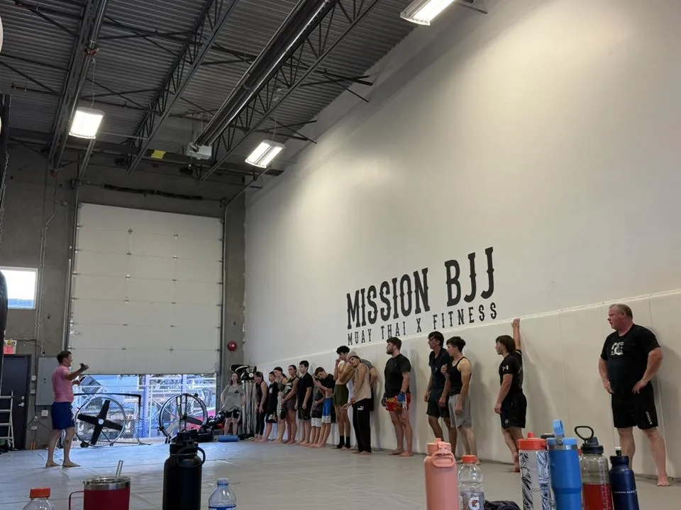 Fighters lined up beneath the Mission BJJ wall logo before training